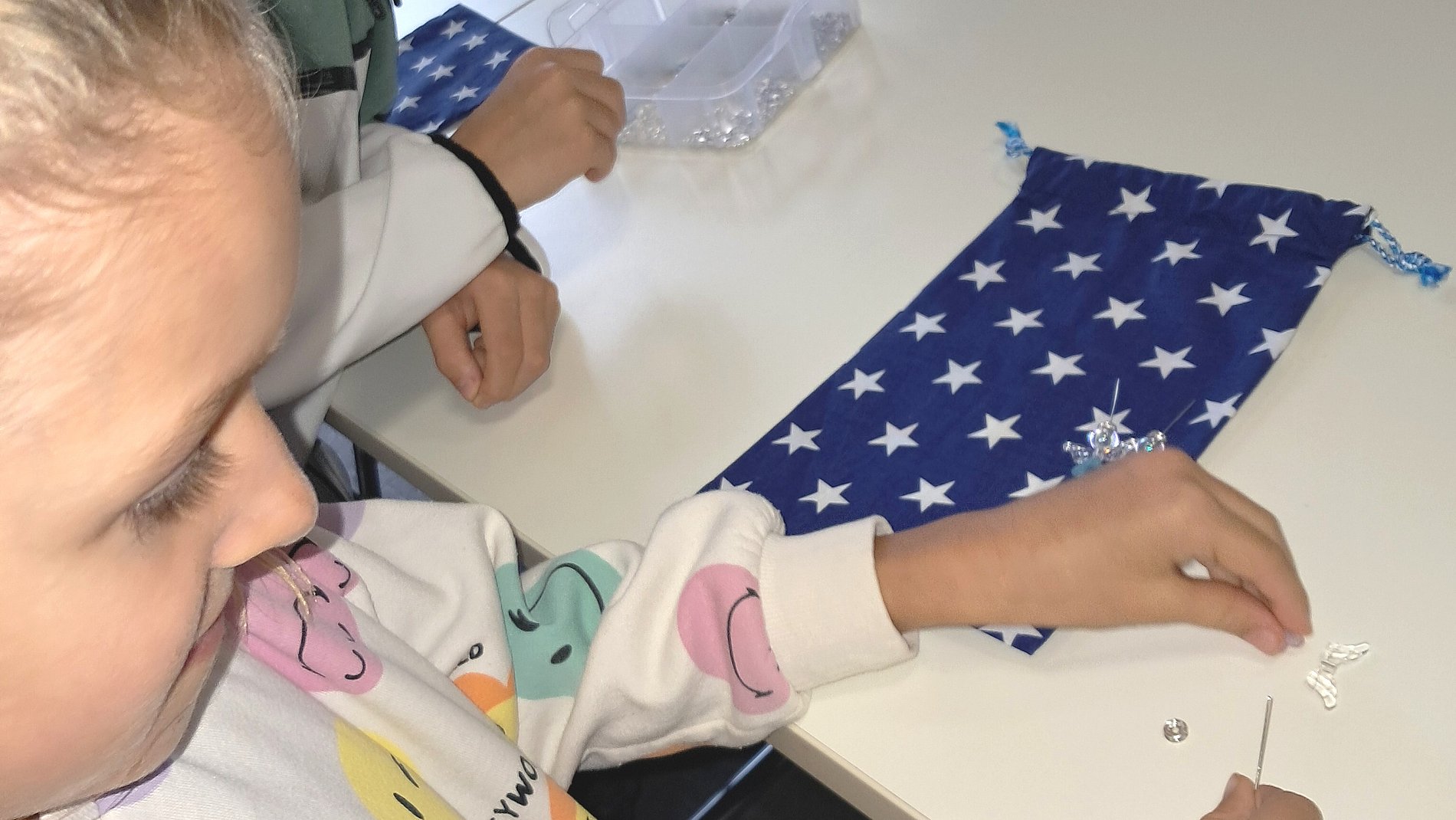 Ein Kommunionkind fädelt Perlen auf.