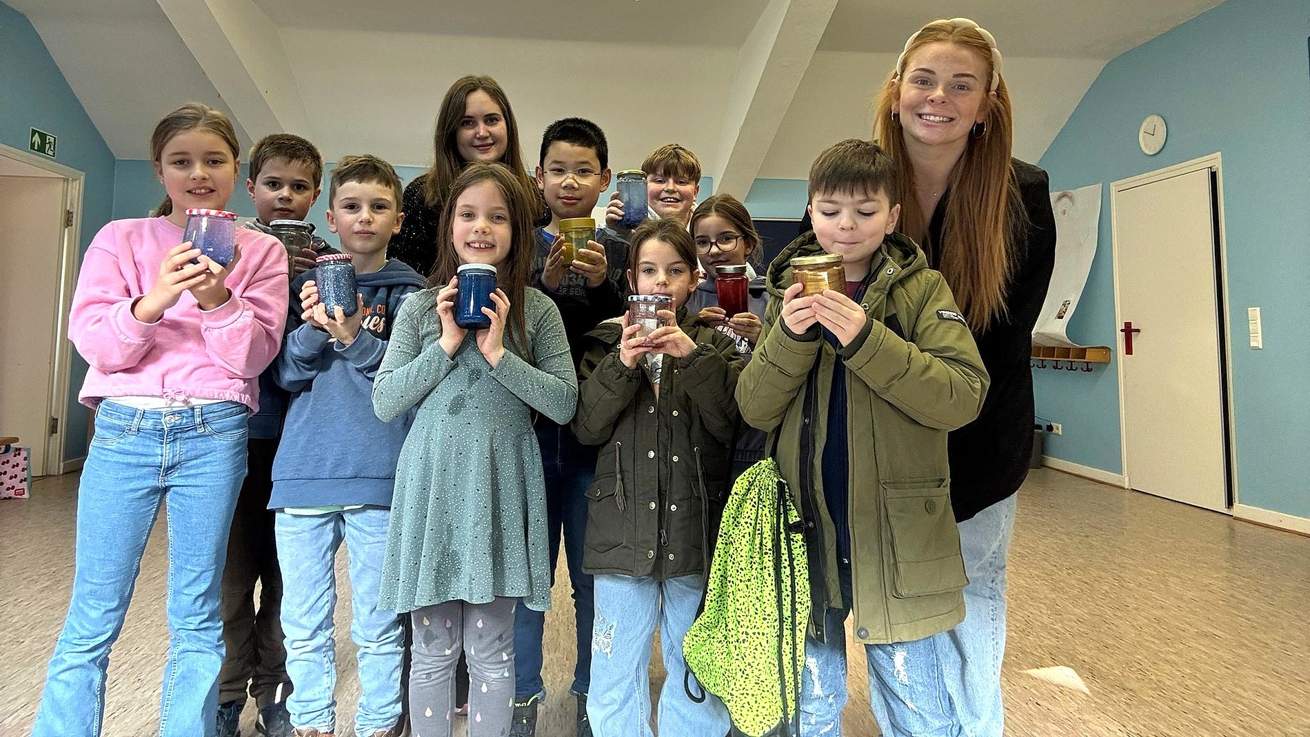 Kommunionkinder stehen in einer Gruppe und halten Gläser mit farbigen, glitzernden Inhalten vor sich