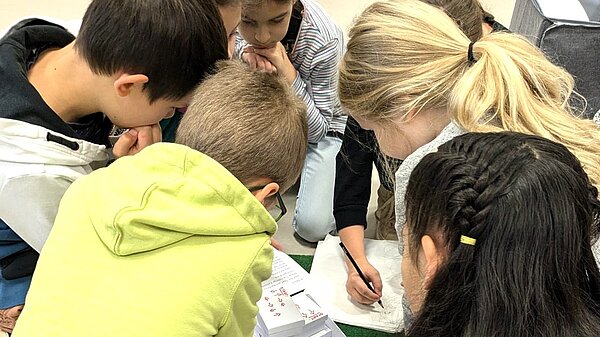 Kommunionkinder stecken die Köpfe zusammen, um ein Rätsel zu lösen