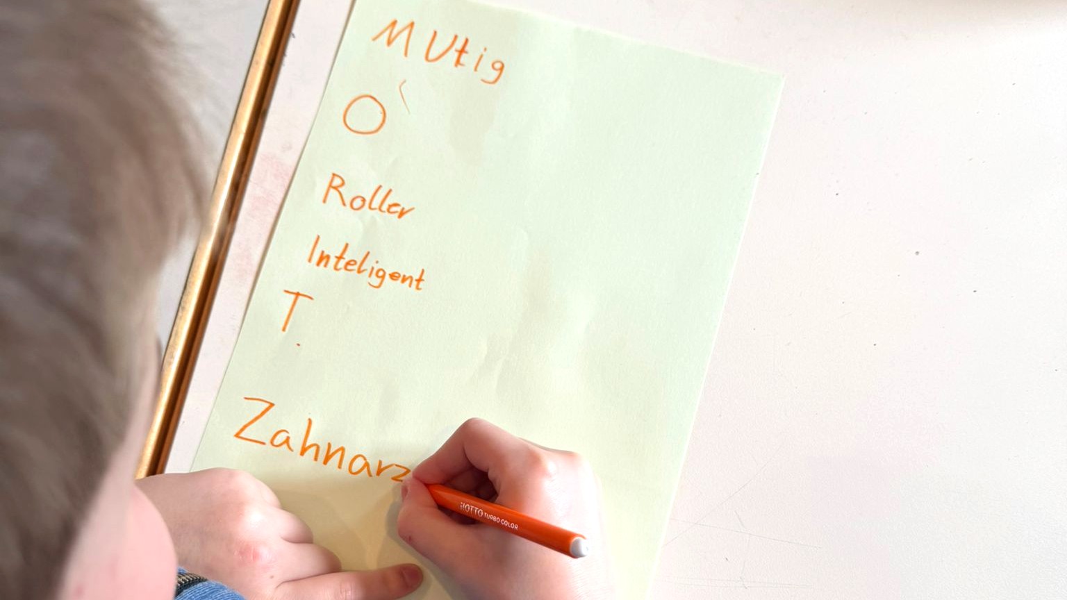 Auf einem Blatt mit seinem Namen schreibt ein Junge Eigenschaften, die mit den Namensbuchstaben beginnen