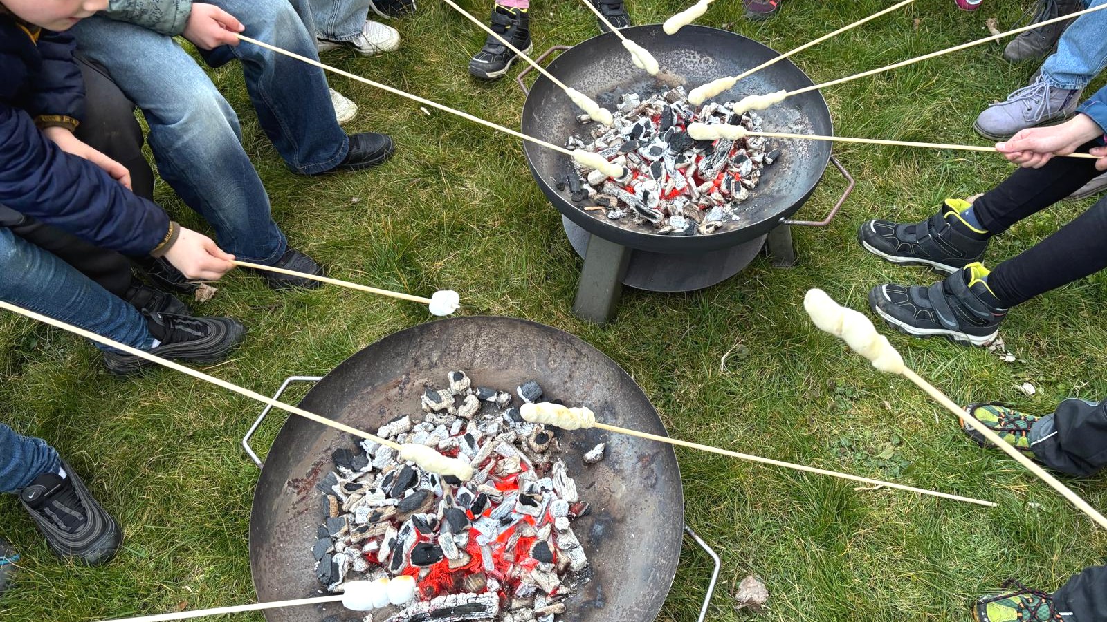 Kommunionkinder rösten Stockbrot über zwei Feuerschalen