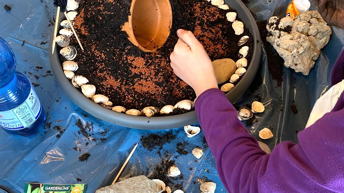 Eine Schale wird mit Erde einem Tontopf und Muscheln gefülklt