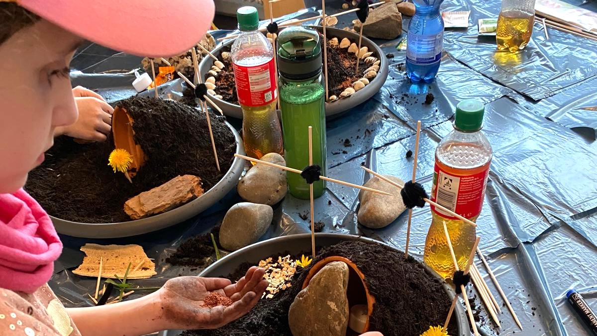 Am Rand der Schale stehen drei Kreuze, geschmückt wird mit farbiger Erde