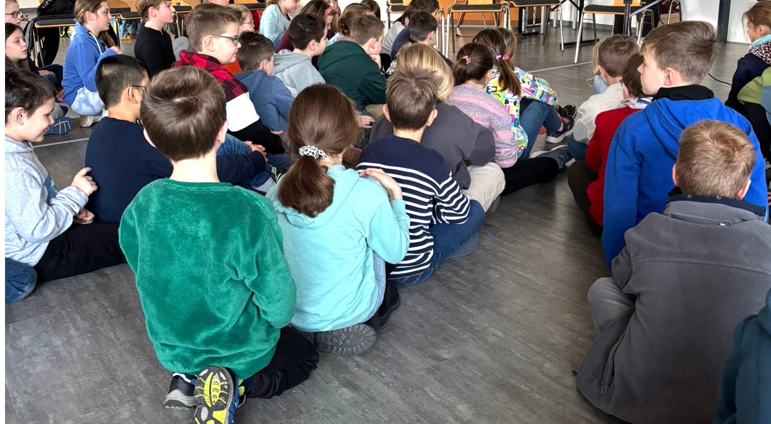 Die Kommunionkinder sitzen in Reihen hintereinander auf dem Boden.