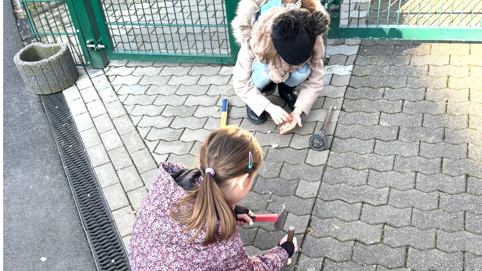 Zwei Mädchen zerschlagen draußen auf dem Pflaster kleine Gegenstände.